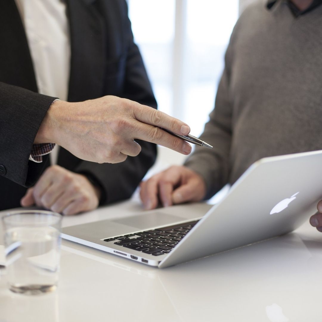 Two people are discussing something on a laptop screen. One person points with a pen.