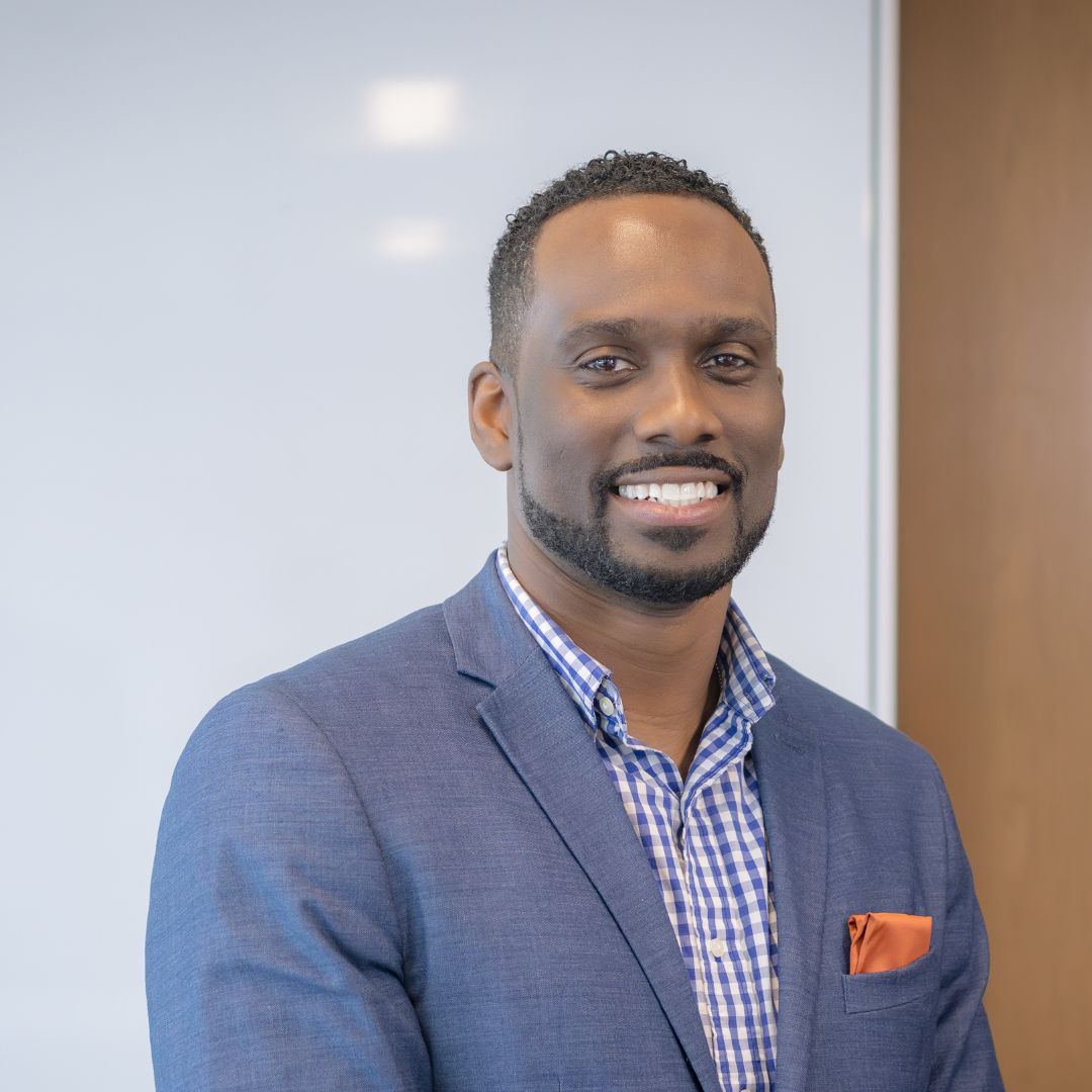 Portrait of Jay Dell, a smiling Black man with short hair and wearing a blue suit.