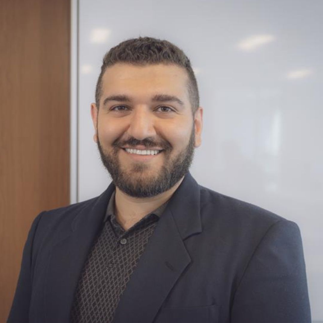 Portrait of Karam Noel, a smiling Middle Eastern man wearing an all-black suit.