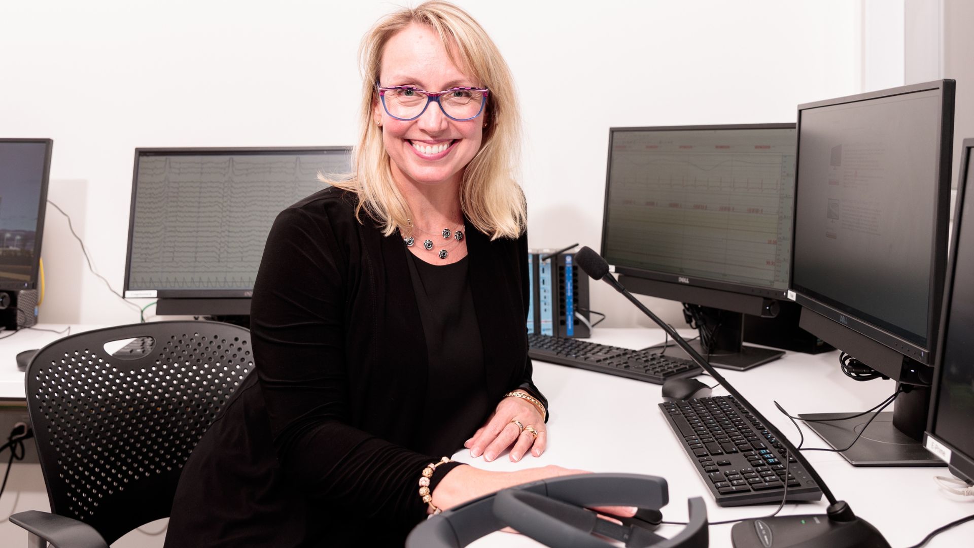DeGroote professor Dr. Millena Head smiles while sitting at a desk surrounded by computer monitors.