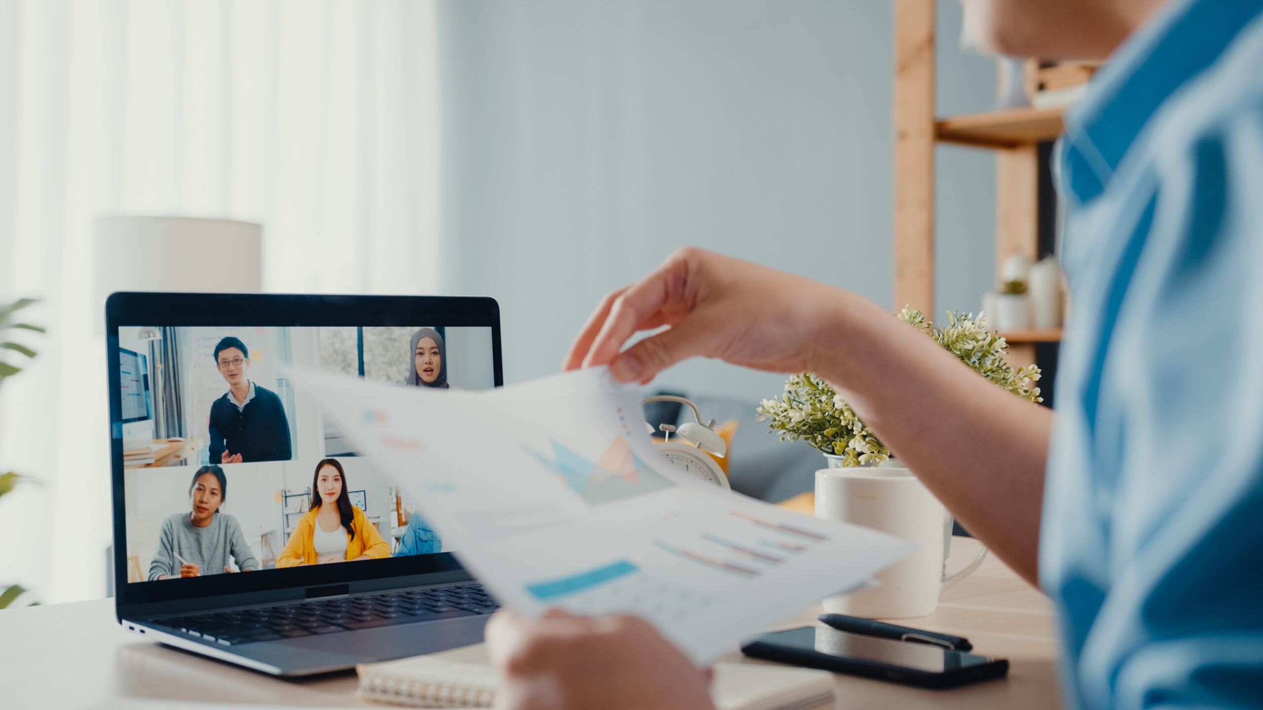 A young Asia businessman using a laptop talks to colleagues about a plan in a video call meeting while working from home in the living room.