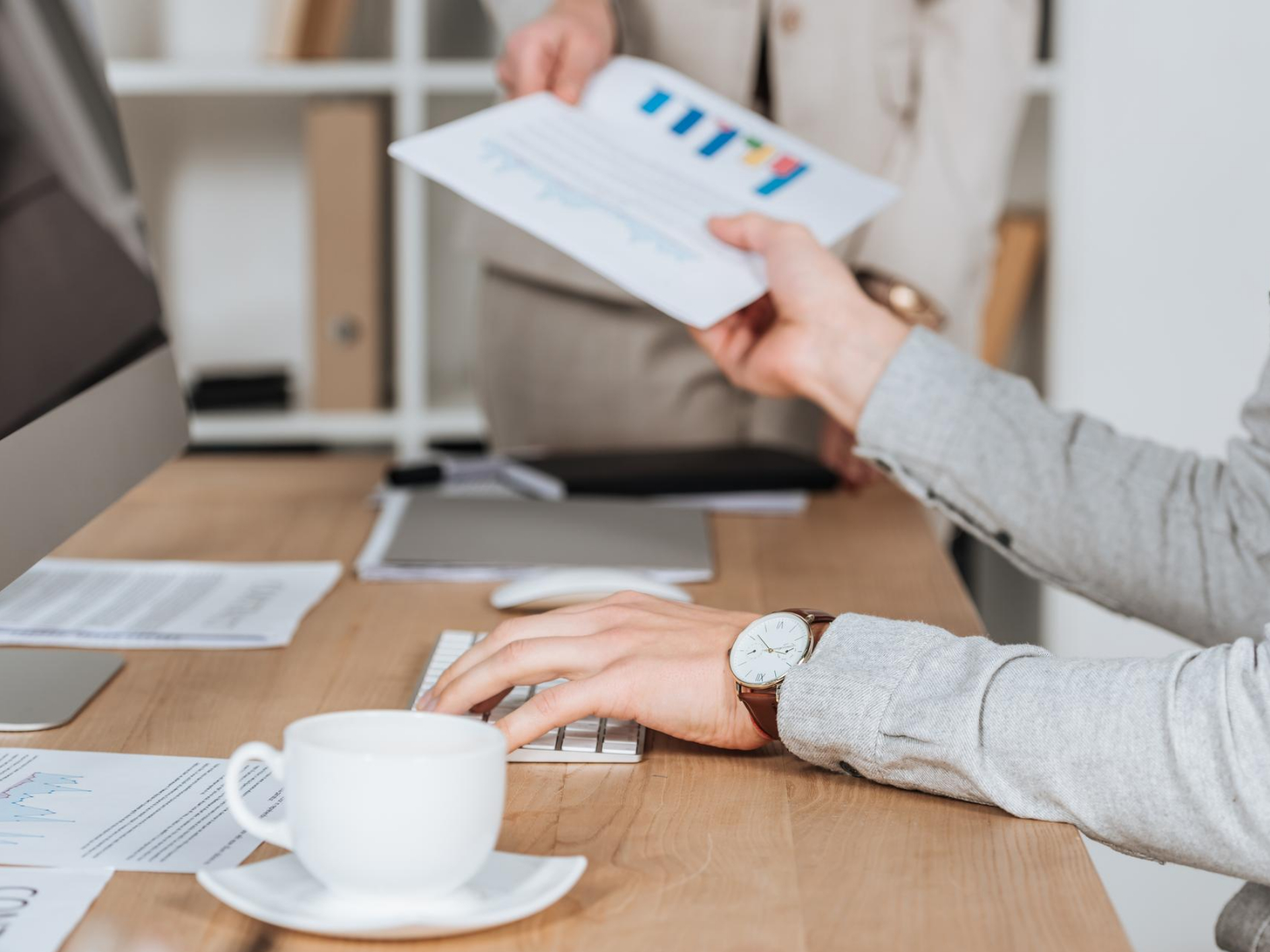 Partial view of business colleagues holding paper with charts and graphs above desk in office