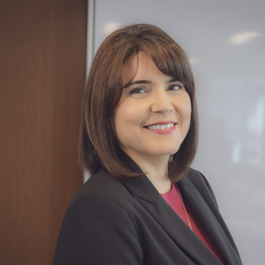 Portrait of Nidia Cerna, a smiling Hispanic woman wearing a black blazer with a red shirt.